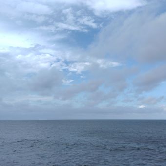 The Blue Horizon, with almost flat ocean below and blue sky chequered with white and grey clouds