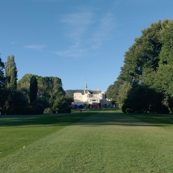 From Dunrossil Drive, with Government House framed between trees to the left and right as well as meticulously mown lawn below and brilliant blue sky above, with Telstra Tower just visible above