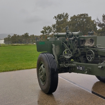Parliamentary Cannon, New Parliament House, with a navy-green slimline military cannon on a trailer pointing towards Old Parliament House in the distance which has Mt Ainslie in the ditance behind it almost covered in low cloud