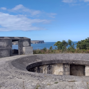 Inner Middle Head Battery, Mosman, with an old for in the foreground dug into the ground, with a stone outpost on the left of the image overlooking the water and North Head in the distance, with streaky clouds in an otherwise blue sky which is reflected in the ocean below