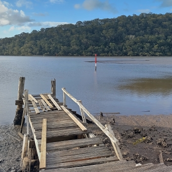 Disused Jetty, Brooklyn, with a delapidated jetty in no fit state for use in the foreground extending from shore to just over the water at low tide, with water reflecting the slightly clouding sky, with low-rolling hills hiding the horizon