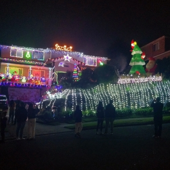 Christmas Lights on Sydney Road, Hornsby Heights, with a two-storey house bordered with lights around every door and window and edge including draped over the hedge at the front of the house