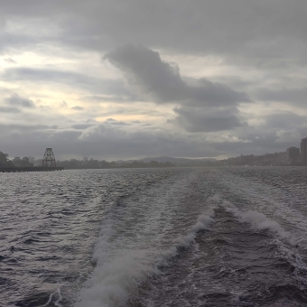 Cloudy Northshore, Hamilton, with choppy waters below made choppier by the trails of the ferry the photo is taken from, with grey clouds gilded by setting sun