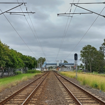 Rail Line Through The Station, Carseldine, with two train lines running towards the horizon, with a station about fifty metres away, with a grey sky