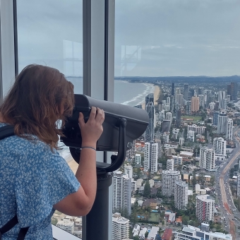 SkyPoint View, Surfers Paradise, with a person looking through binoculars down at other not-so-tall buildings from seventy storeys up, with a beach visible as a small strip to the left and bushland mountains off in the far distance