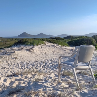 The Throne Of The Dunes, Bennetts Beach, Hawks Nest, with a cheap yet padded chair facing away and over yellow then plant-covered dunes which eventually turn into a bay with low mountains on the other side, with clear blue sky above