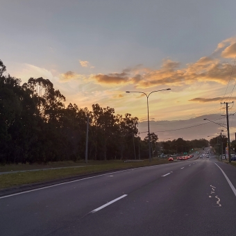 Sunset on Deception Bay Road, Deception Bay, with a road going from centre frame to back right with no cars, with barely grey clouds gilded with setting sun filling half the sky