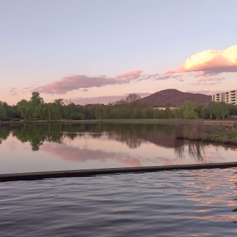 Nerang Pool, Parkes, withgreen trees and gilded peach-coloured clouds reflected in the clear water