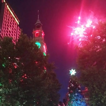 An Early Christmas Celebration, Martin Place, with the Post Office on the left lit up with red and green lights, with the clock tower in the centre similarly adorned, with a Christmas tree and red fireworks on the right