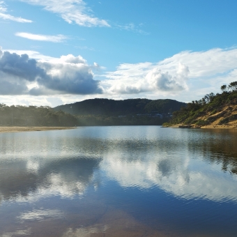 Distant Pelicans, Wamberal Lagoon, Wamberal, with a flat lagoon reflecting blue sky and rolling hills and three pelicans in the distance