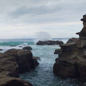 A Waving Break, Sea Cave, Caves Beach, with a wave breaking over a protruding rock which is all surrounded by water then more rocks