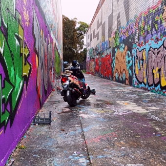 Derelict Dumping, Lilian Fowler Walkway, Marrickville, with a dilapidated motorbike in the middle of a walkway, with graffiti covered both left and right walls