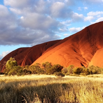 Uluṟu, The Eastern Face, with sun and cloud-shadow strewn across the slope of Uluru which extends from top right to bottom left