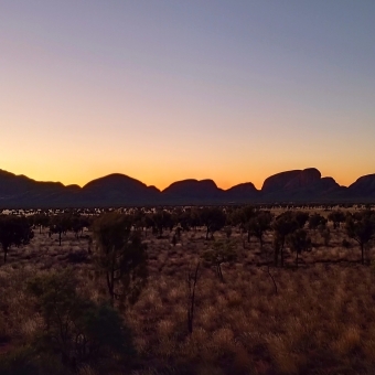 Kata Tjuṯa, Sunset from the Dune Viewing Area, with orange and peach and pastel-pink and pastel-blue glowing behind the silhouette of many heads of the rock formation
